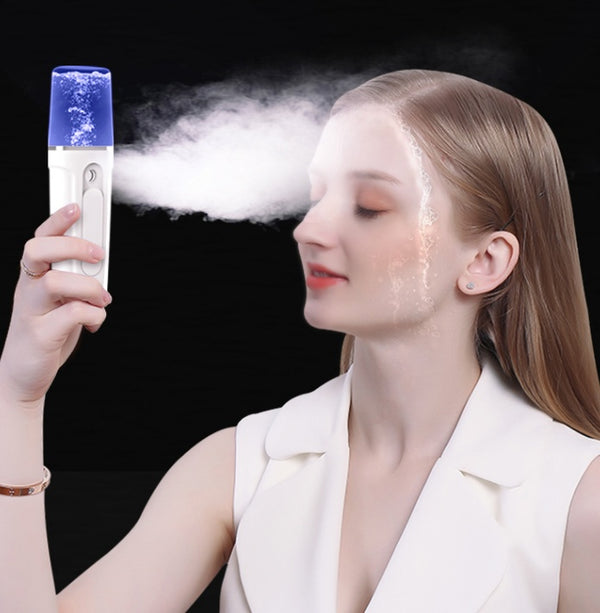Person using a handheld device to mist their face with steam against a black background