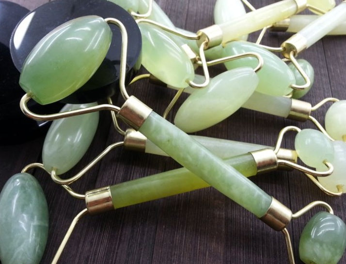 Green jade rollers with gold accents on a dark surface