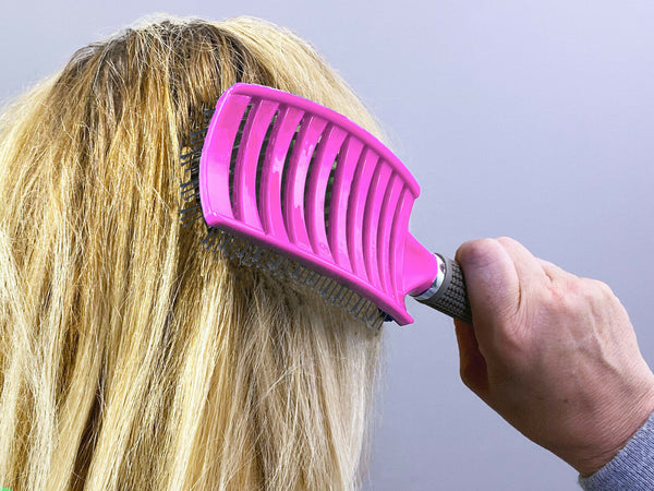 Person using a pink pet grooming brush on their hair against a gray background