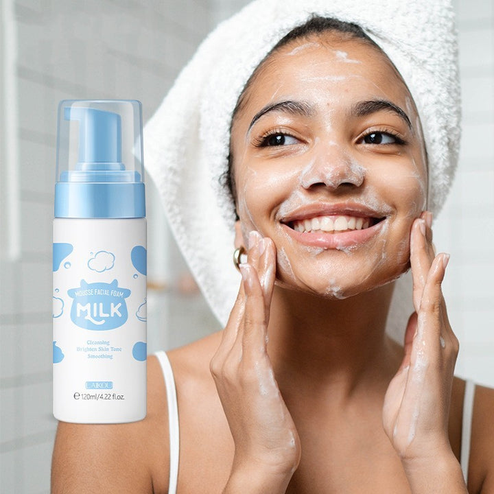Woman applying facial foam with a bottle of 'Milk' brand product next to her.